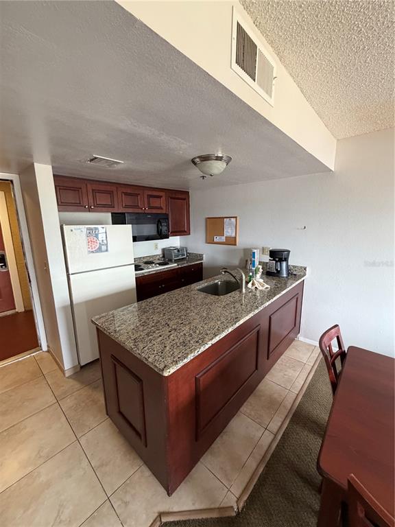 A kitchen features a granite-topped island, dark wood cabinetry, and tile flooring — 6403 PARC CORNICHE DRIVE UNIT 4305, ORLANDO, FL