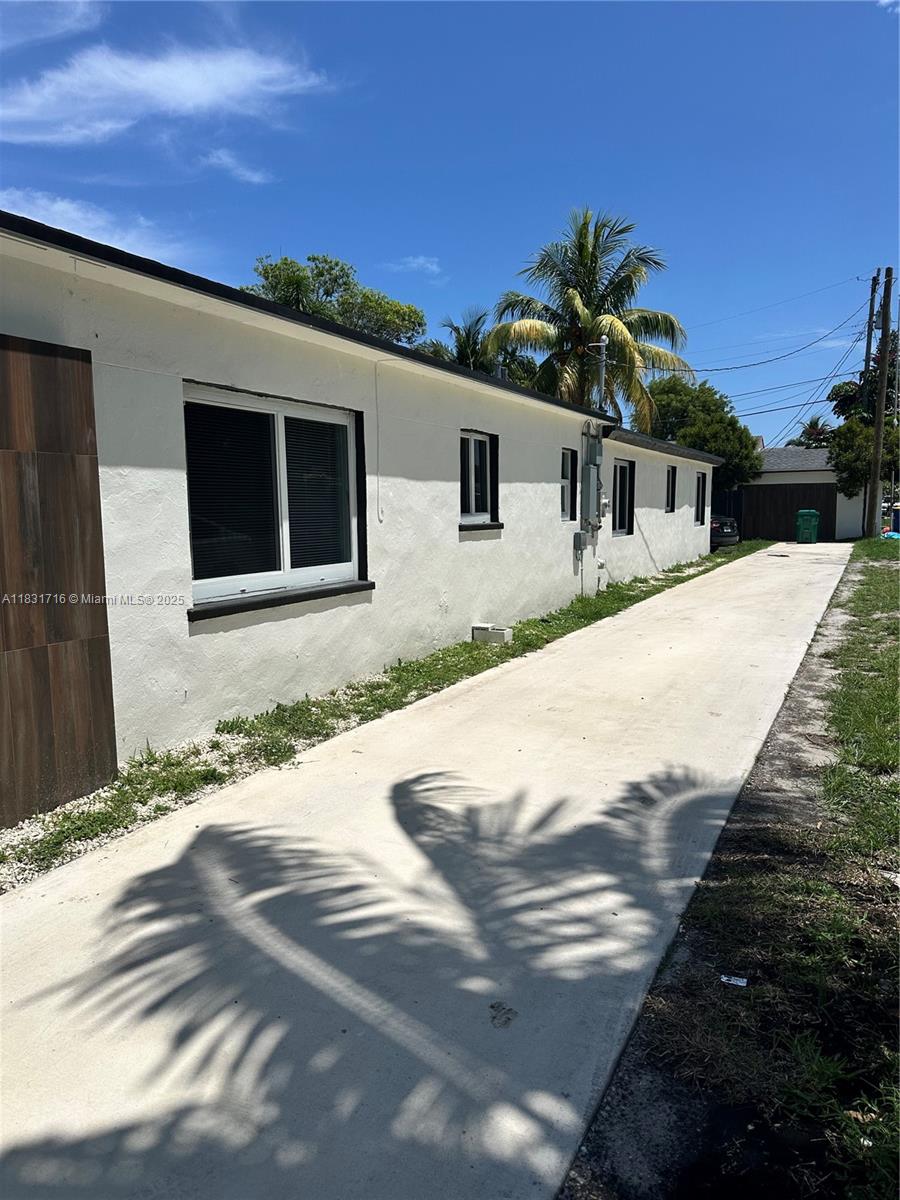 A long concrete driveway runs alongside the white exterior wall of a single-story house — 42 SE 10th Ter, Dania Beach FL 33004, DANIA BEACH, FL