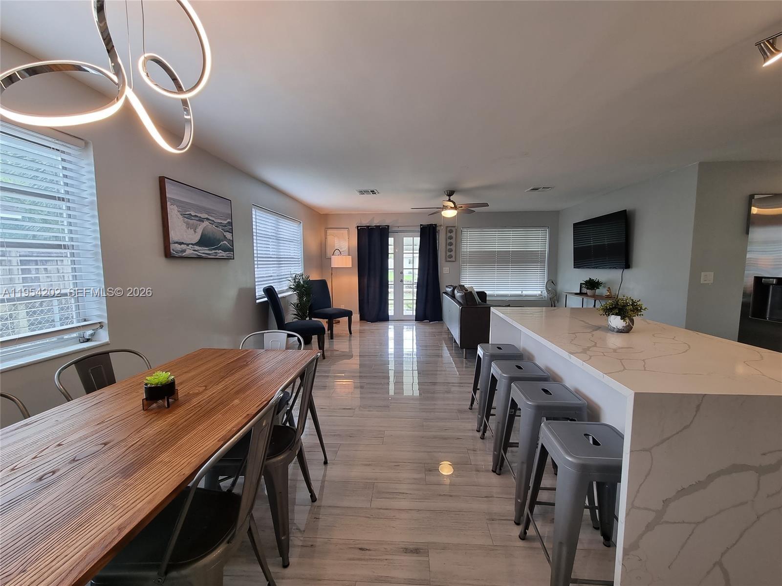 An open-concept dining and kitchen area features a wooden table, island seating, and tiled floors — 4740 SW 43rd Ave, Dania Beach FL 33314, DANIA BEACH, FL
