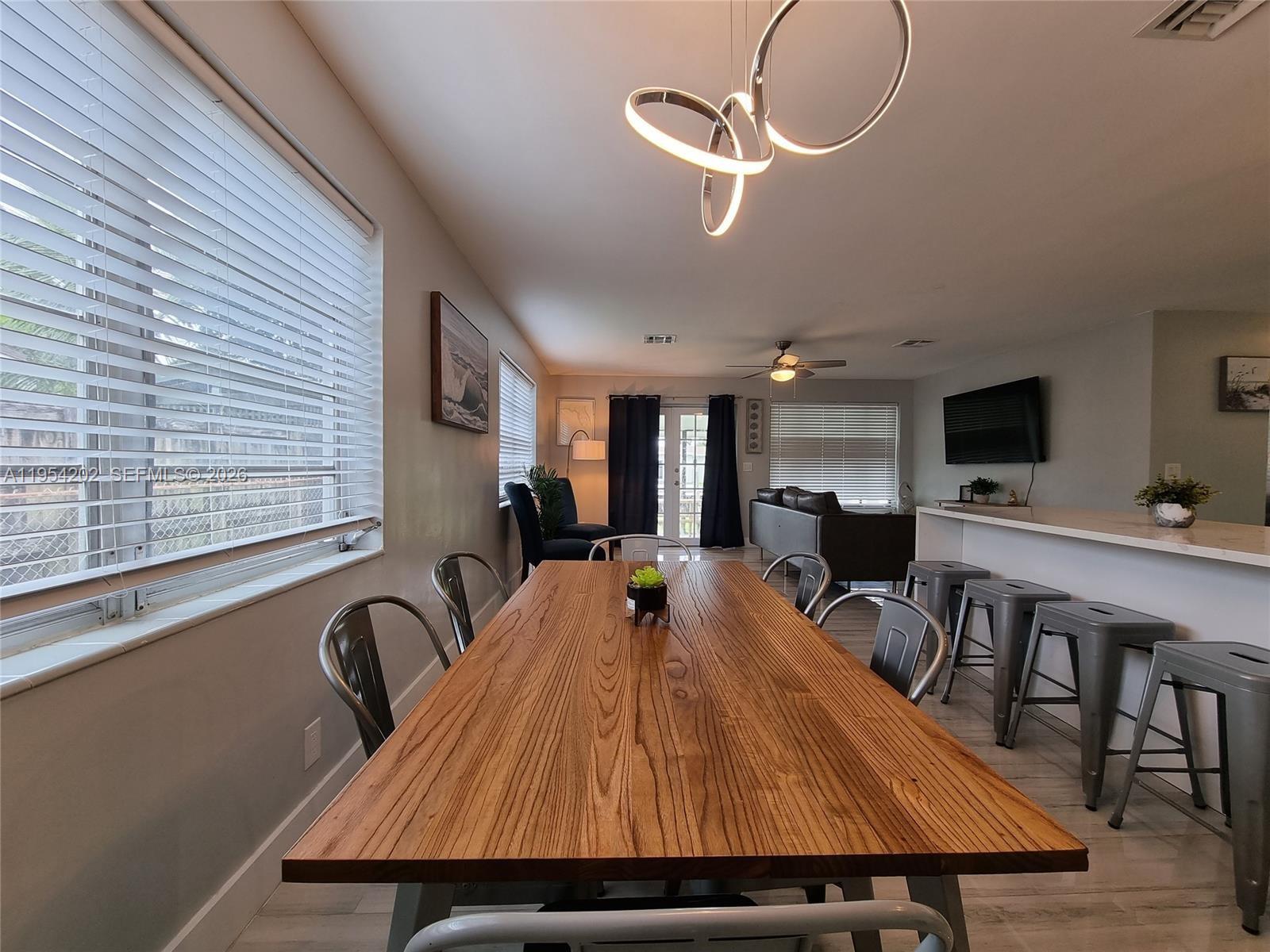 A dining area with a wooden table and metal chairs sits before an open living room — 4740 SW 43rd Ave, Dania Beach FL 33314, DANIA BEACH, FL