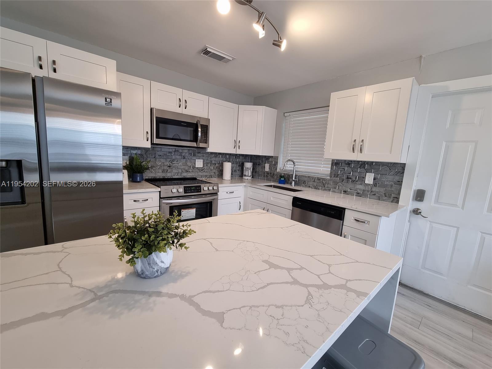 A modern kitchen features white cabinets, a large quartz island, and a gray tiled backsplash — 4740 SW 43rd Ave, Dania Beach FL 33314, DANIA BEACH, FL