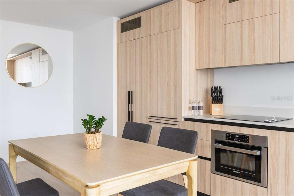 A modern kitchen features light wood cabinetry, a dining table, and built-in stainless steel appliances — 225 N MIAMI AVENUE UNIT 1407, MIAMI, FL