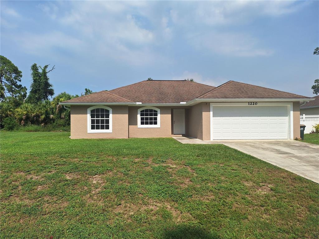 A single-story tan house with a brown roof, white trim, and a two-car garage — 1220 WAYCROSS STREET, NORTH PORT, FL