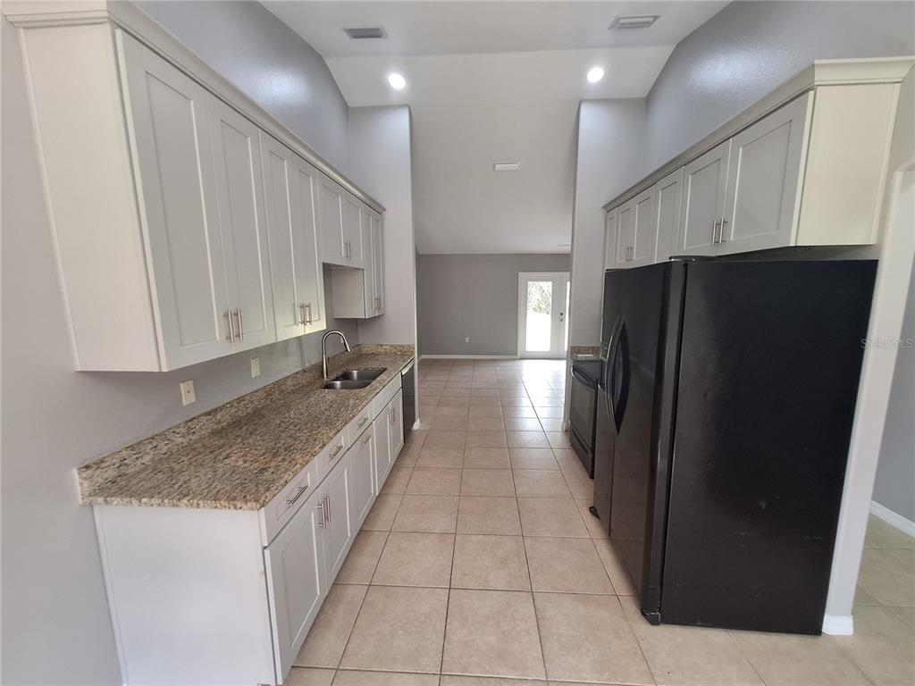 A galley-style kitchen features light gray cabinets, granite countertops, and black appliances — 1220 WAYCROSS STREET, NORTH PORT, FL