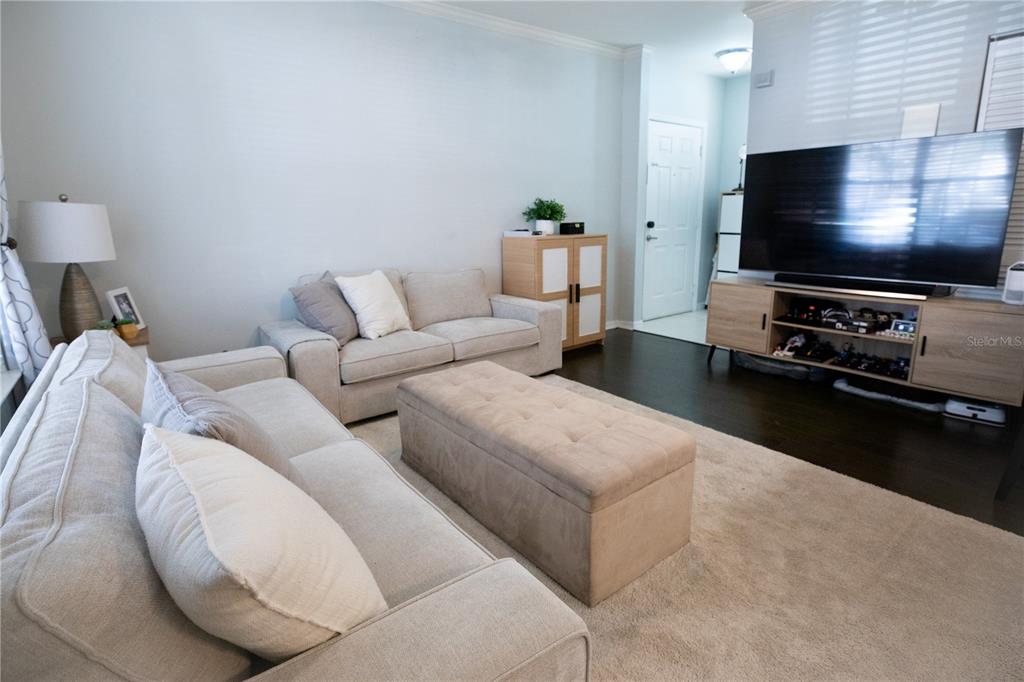 A living room features light-colored sofas, a tufted ottoman, and a large television on a stand — 1020 SIENA PARK BOULEVARD W UNIT # 103, CELEBRATION, FL