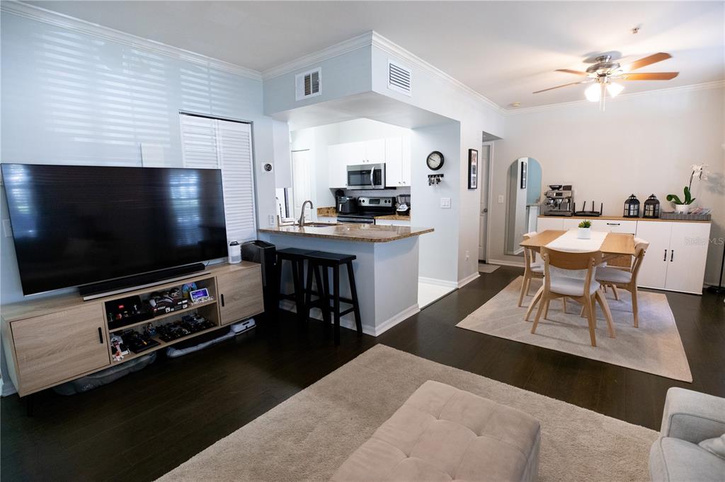 An open-concept living and dining area features dark wood floors, a kitchen island, and furniture — 1020 SIENA PARK BOULEVARD W UNIT # 103, CELEBRATION, FL