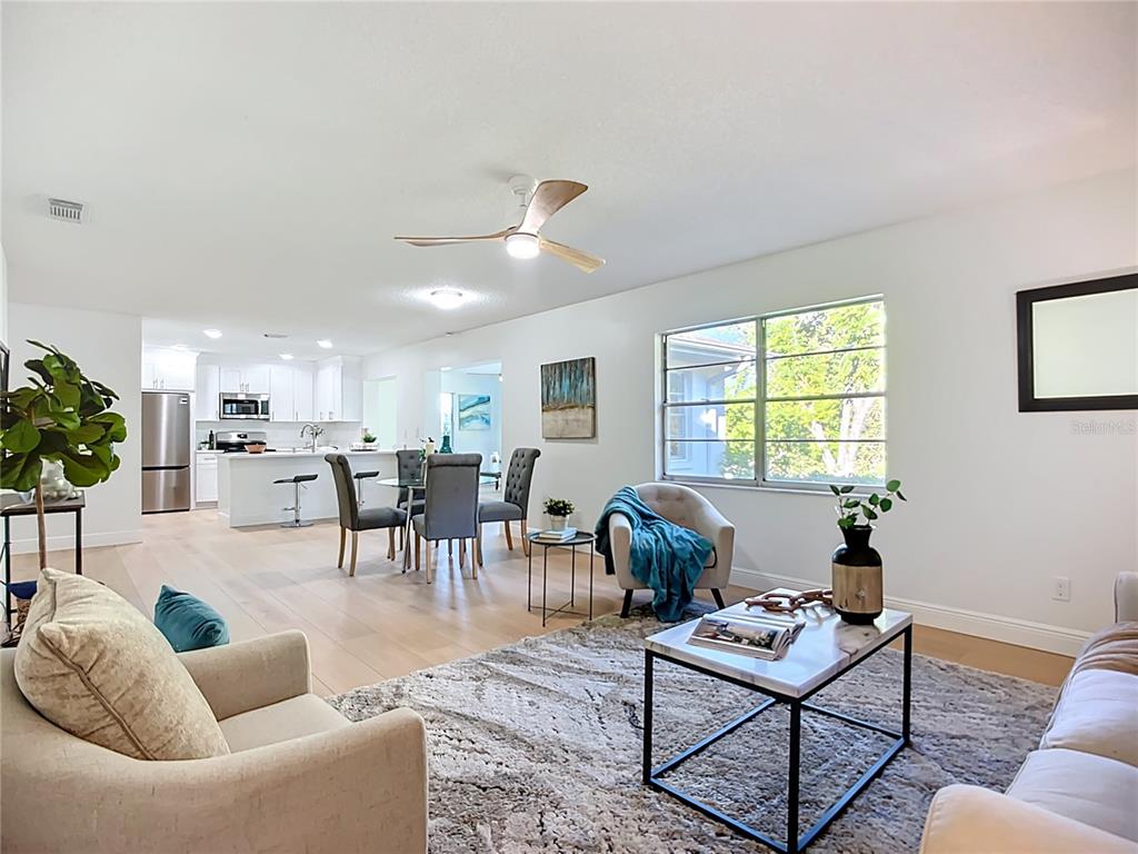 An open-concept living and dining area features light wood flooring, white walls, and modern furniture — 2014 HAMPSTEAD CIRCLE, SUN CITY CENTER, FL