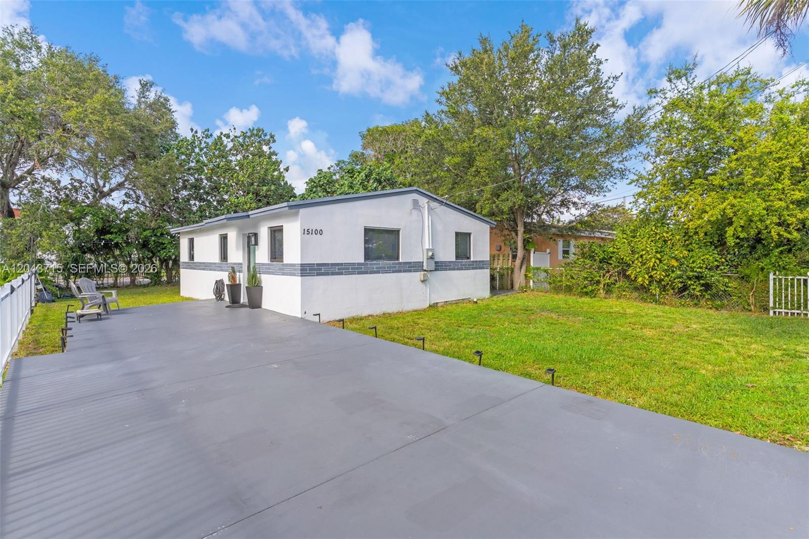 A white single-story house with a gray trim band sits beside a large paved patio — 15100 NE 14th Ct, North Miami Beach FL 33162, NORTH MIAMI BEACH, FL