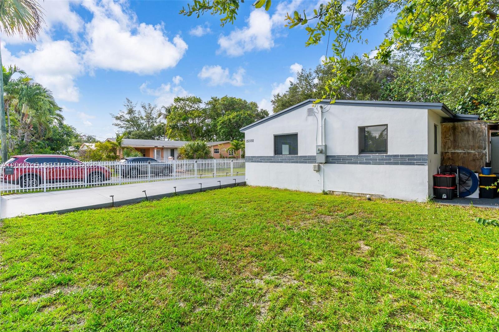 A white single-story house with a gray accent stripe sits next to a grassy yard — 15100 NE 14th Ct, North Miami Beach FL 33162, NORTH MIAMI BEACH, FL
