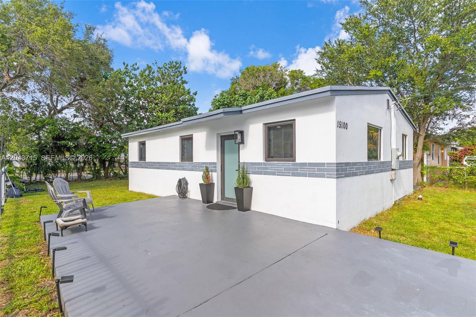 A white house with a gray horizontal accent stripe features a concrete patio and chairs — 15100 NE 14th Ct, North Miami Beach FL 33162, NORTH MIAMI BEACH, FL