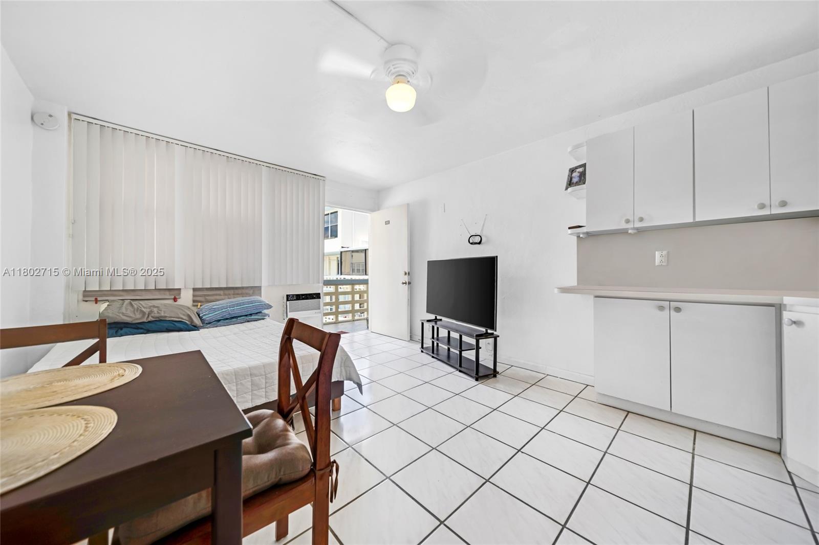 A studio apartment features white tile floors, a small kitchenette, and a bed near a balcony — 6484 Indian Creek Dr # 202, Miami Beach FL 33141, MIAMI BEACH, FL