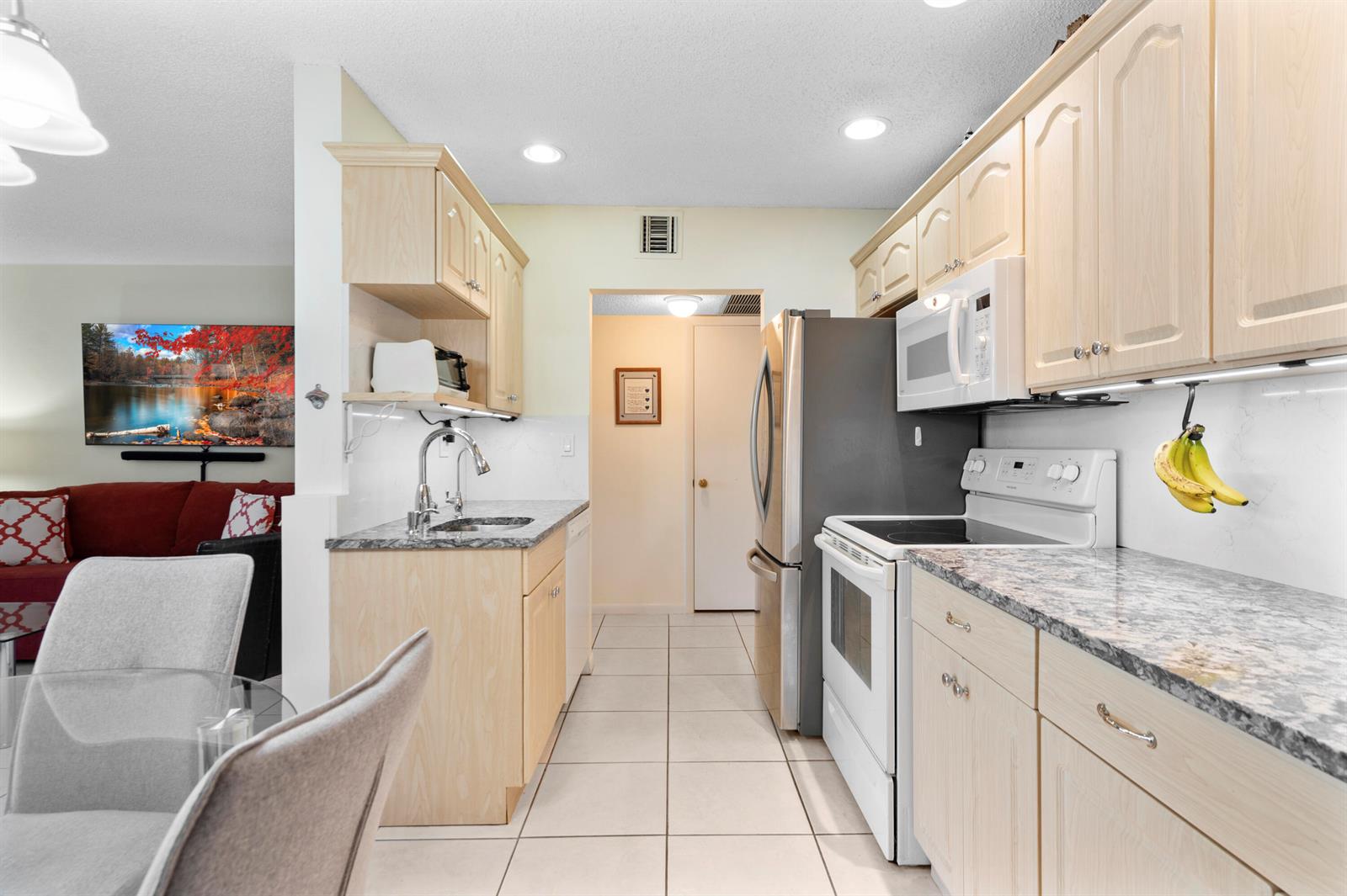 A kitchen features light wood cabinets, granite countertops, white appliances, and tile flooring — 5180 E Sabal Palm Boulevard # 234, Tamarac FL 33319, TAMARAC, FL