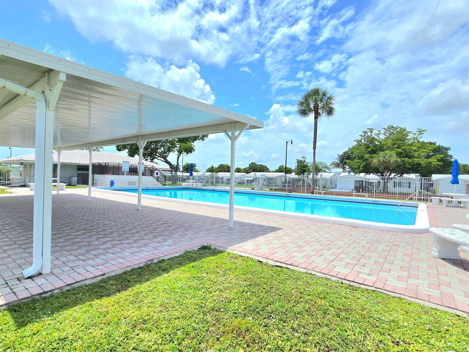 A rectangular swimming pool sits beside a covered patio area with brick pavers — 2501 W Golf Boulevard # 127, Pompano Beach FL 33064, POMPANO BEACH, FL