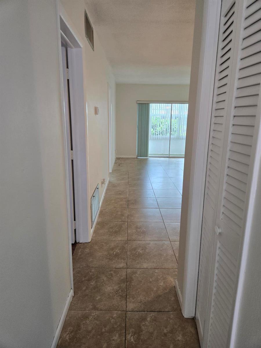 A hallway with tile flooring leads toward a living area with a sliding glass door — 2501 W Golf Boulevard # 127, Pompano Beach FL 33064, POMPANO BEACH, FL