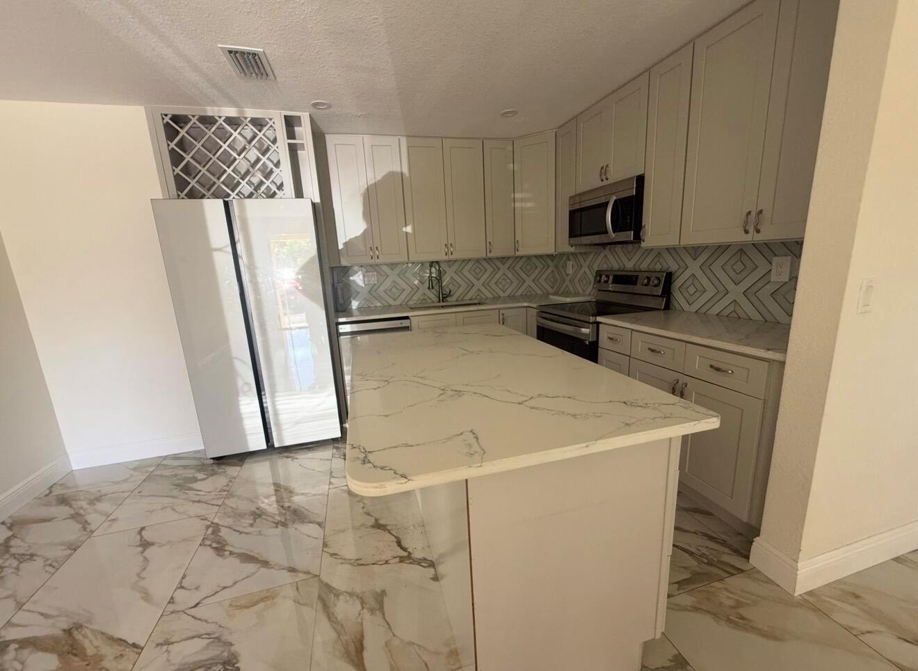 A modern kitchen features light gray cabinets, a marble-patterned island, and matching tile flooring — 2122 NE 1st Street, Boynton Beach FL 33435, BOYNTON BEACH, FL