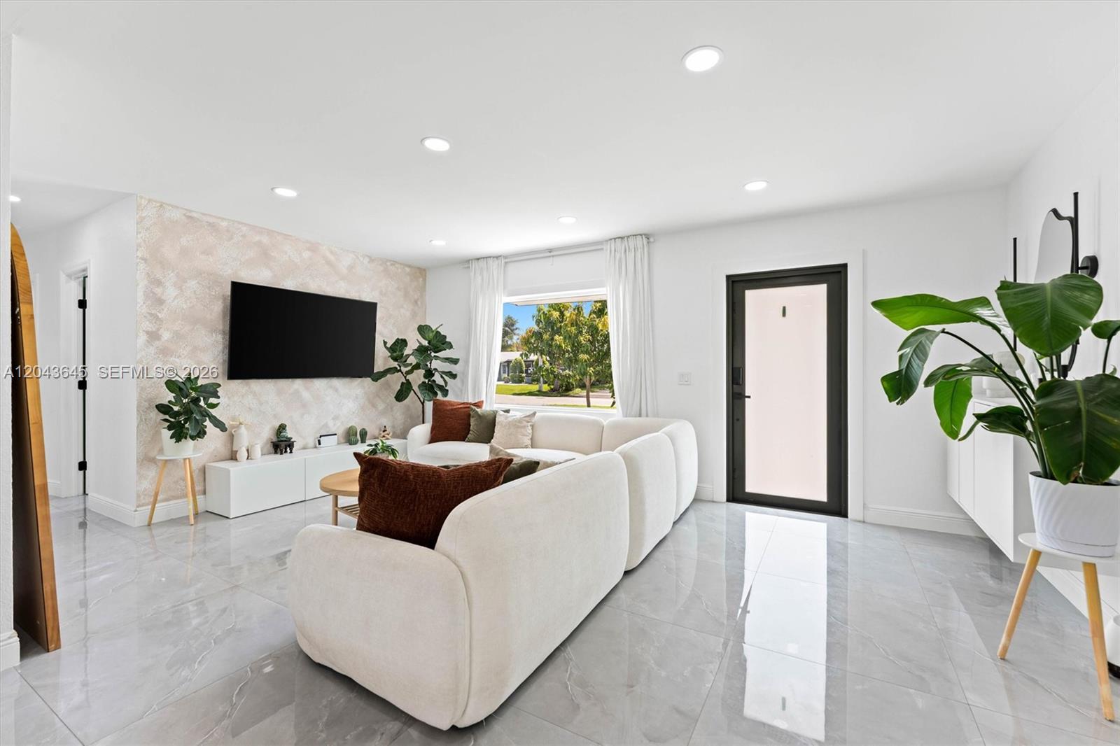 A bright living room features a white sectional sofa, a textured accent wall, and tile flooring — 1120 SW 7th Ave, Deerfield Beach FL 33441, DEERFIELD BEACH, FL
