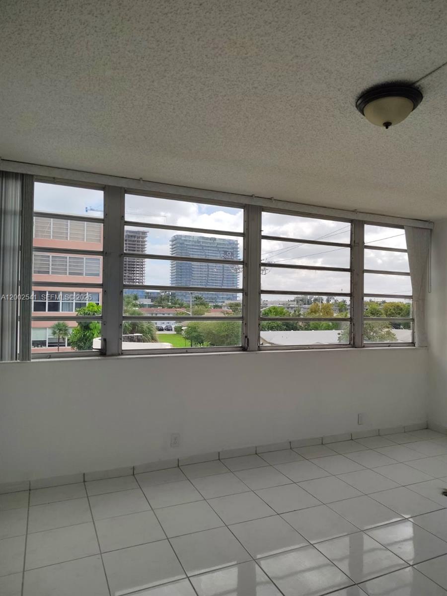 An interior room with white tile flooring and large windows overlooking a city skyline — 200 NE 12th Ave # 1C, Hallandale Beach FL 33009, HALLANDALE BEACH, FL