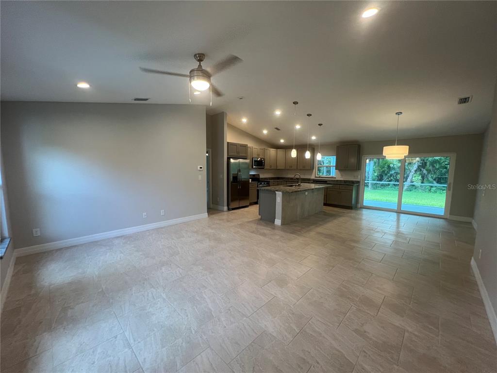An open-concept kitchen and living area features tile flooring, stainless steel appliances, and sliding doors — 2451 WALLER ROAD, NORTH PORT, FL