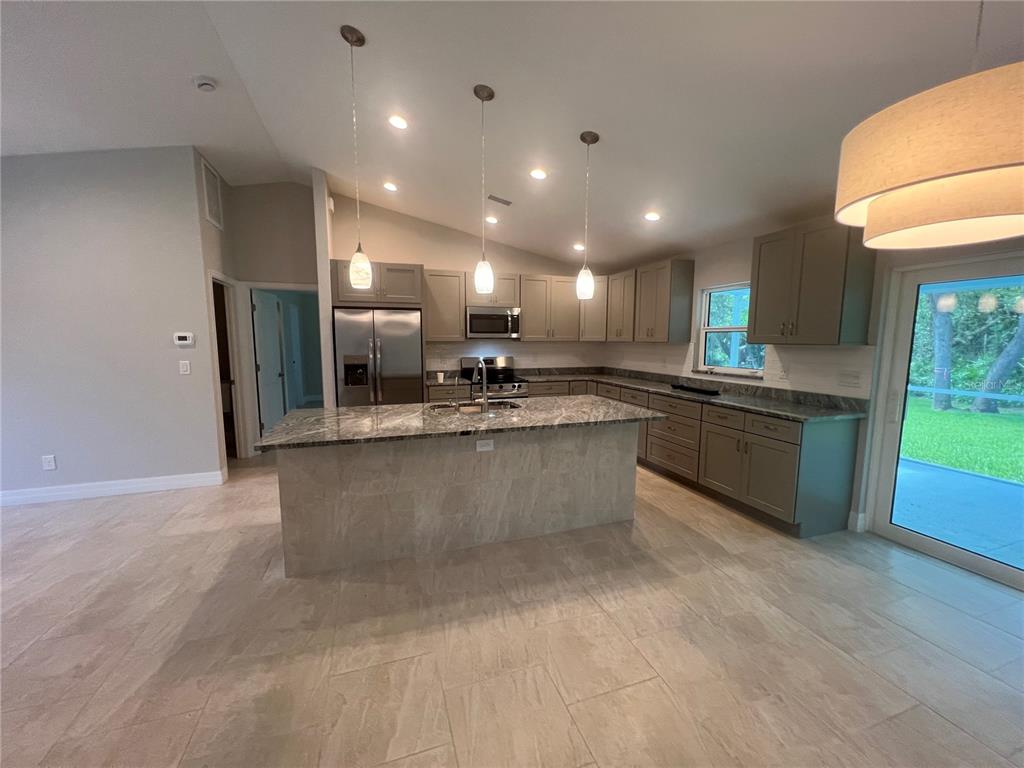 A kitchen features a granite-topped island, gray cabinetry, stainless steel appliances, and tile flooring — 2451 WALLER ROAD, NORTH PORT, FL