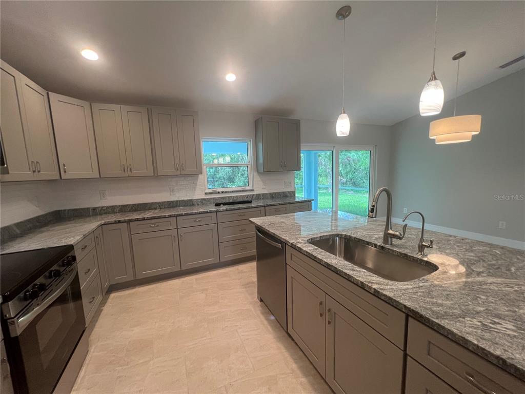 A kitchen features gray cabinetry, granite countertops, a center island with a sink, and tile flooring — 2451 WALLER ROAD, NORTH PORT, FL