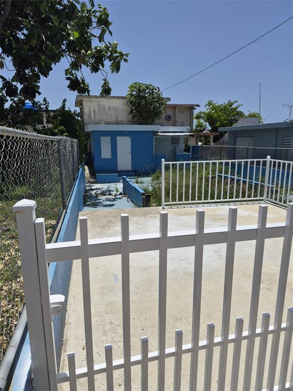 A blue house with a white door sits behind a white metal fence and gate — 1 BARRIO MORA, ISABELA, PR