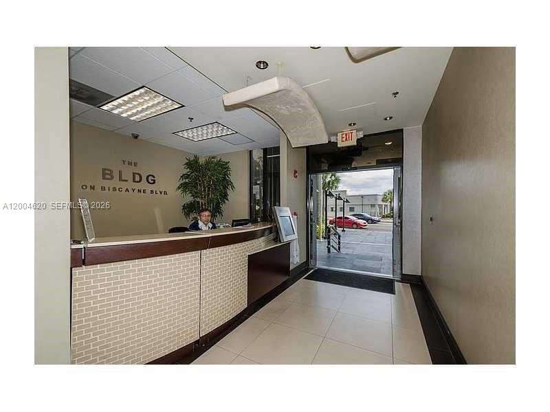 A reception desk with a person sits in a lobby with a glass exit door — 12550 Biscayne Blvd UNIT 403, North Miami FL 33181, NORTH MIAMI, FL