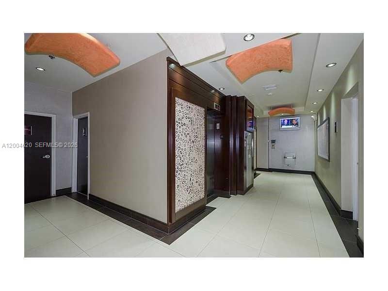 A modern building lobby features an elevator bank with decorative paneling and tile flooring — 12550 Biscayne Blvd UNIT 403, North Miami FL 33181, NORTH MIAMI, FL