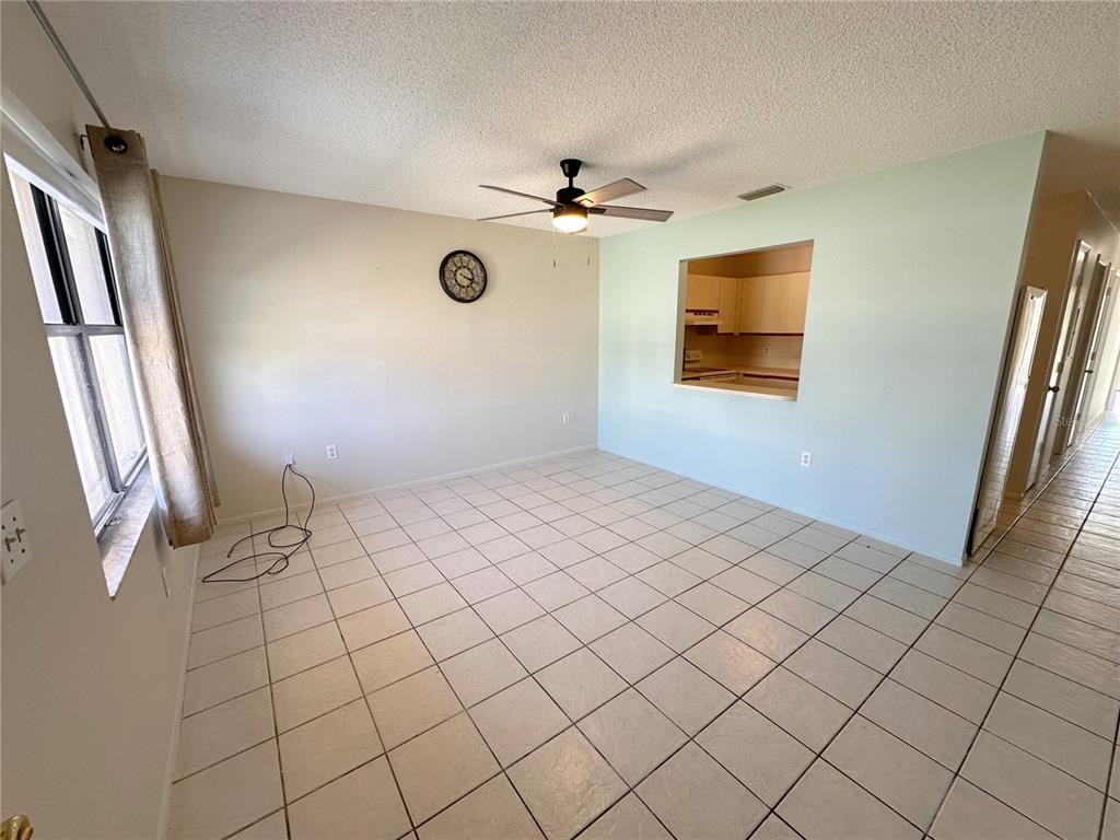An empty room with tiled floors, a ceiling fan, and a pass-through window to the kitchen — 77 BOUNDARY BOULEVARD UNIT B, ROTONDA WEST, FL