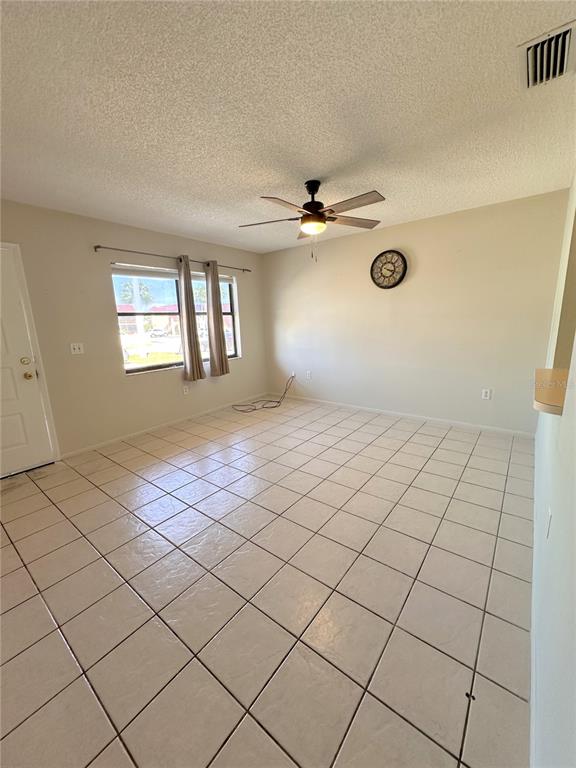 A living room with light-colored tile flooring, a ceiling fan, and a window with curtains — 77 BOUNDARY BOULEVARD UNIT B, ROTONDA WEST, FL