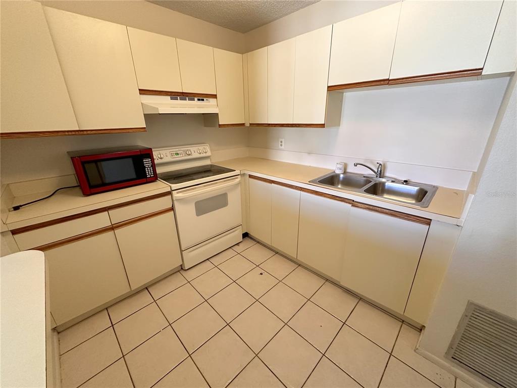 A kitchen features white flat-panel cabinets, a white stove, a red microwave, and tiled flooring — 77 BOUNDARY BOULEVARD UNIT B, ROTONDA WEST, FL