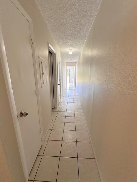 A long hallway with white walls, a textured ceiling, and light-colored square floor tiles — 77 BOUNDARY BOULEVARD UNIT B, ROTONDA WEST, FL