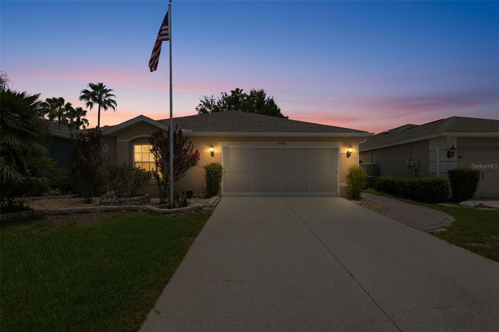 A single-story house with a two-car garage and an American flag at dusk — 10340 BUNCOMBE WAY, SAN ANTONIO, FL
