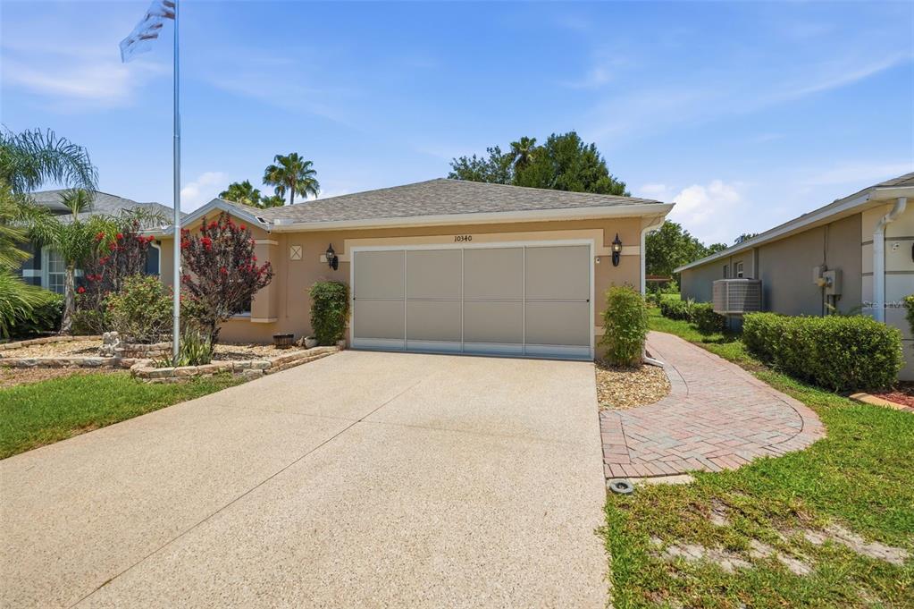 A single-story house with a beige stucco exterior, a two-car garage, and a brick walkway — 10340 BUNCOMBE WAY, SAN ANTONIO, FL