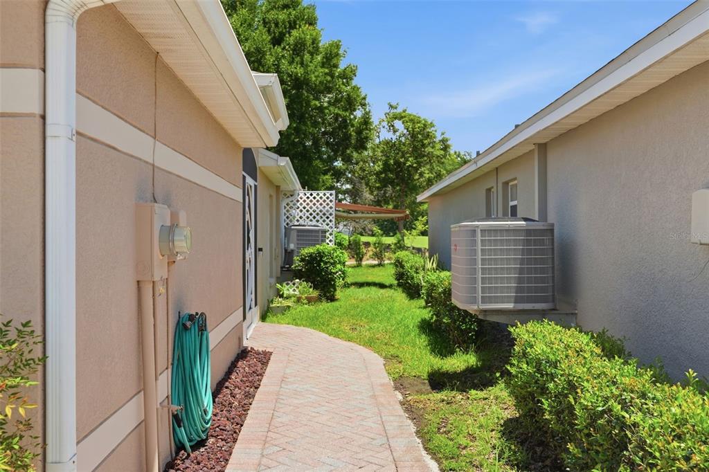 A paved walkway leads between two beige houses with air conditioning units and green landscaping — 10340 BUNCOMBE WAY, SAN ANTONIO, FL