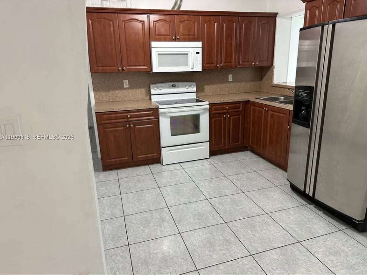 A kitchen features wood cabinets, a white stove, a microwave, and stainless steel appliances — 9021 SW 30th Ter, Miami FL 33165, MIAMI, FL