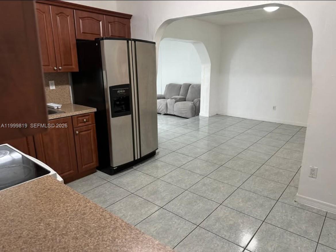 A kitchen with wood cabinets and stainless steel appliances opens into a tiled living area — 9021 SW 30th Ter, Miami FL 33165, MIAMI, FL