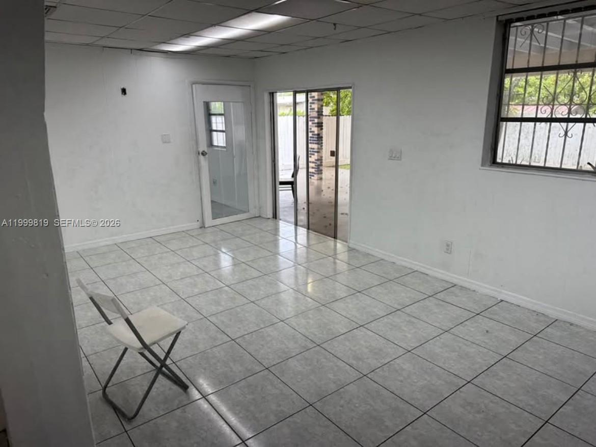 An empty room features white walls, light-colored tile flooring, a sliding glass door, and windows — 9021 SW 30th Ter, Miami FL 33165, MIAMI, FL