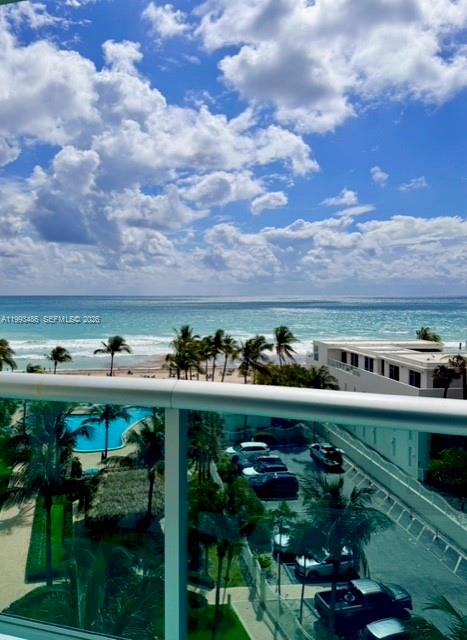 An elevated view shows a beach, ocean, and palm trees beyond a glass balcony railing — 3901 S Ocean Dr # 7M, Hollywood FL 33019, HOLLYWOOD, FL