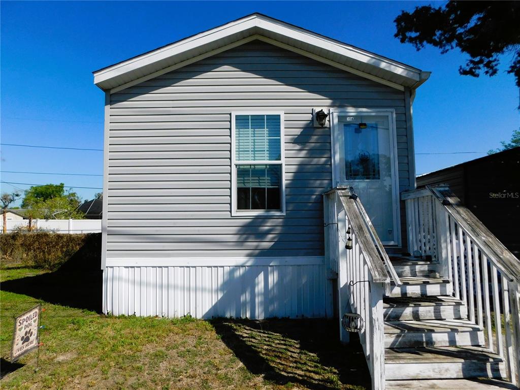 The exterior of a gray, single-story manufactured home features white skirting and wooden stairs — 39143 HILLCREST DRIVE, ZEPHYRHILLS, FL