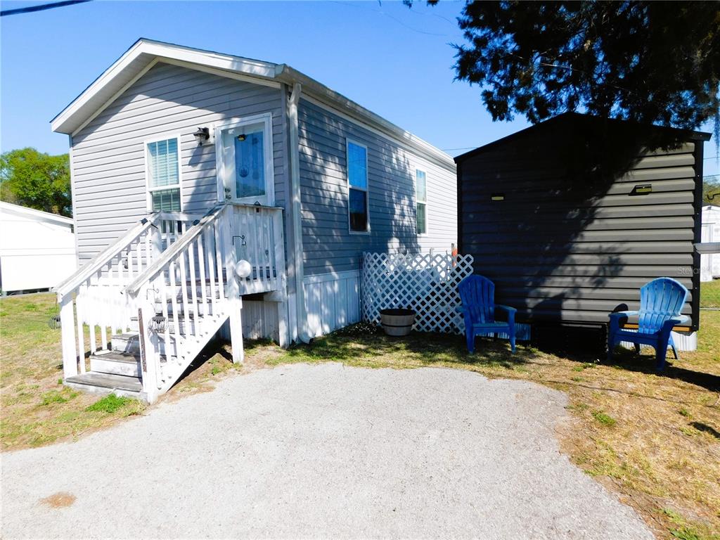 A light gray mobile home with a white staircase sits next to a dark shed — 39143 HILLCREST DRIVE, ZEPHYRHILLS, FL
