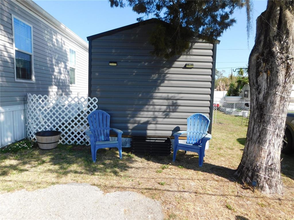 Two blue plastic chairs sit on a lawn in front of a gray shed — 39143 HILLCREST DRIVE, ZEPHYRHILLS, FL