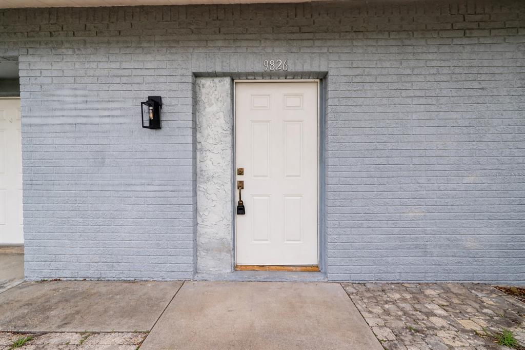 A white front door with a black lockbox is set into a gray brick wall — 9826 POCONO STREET, PORT RICHEY, FL