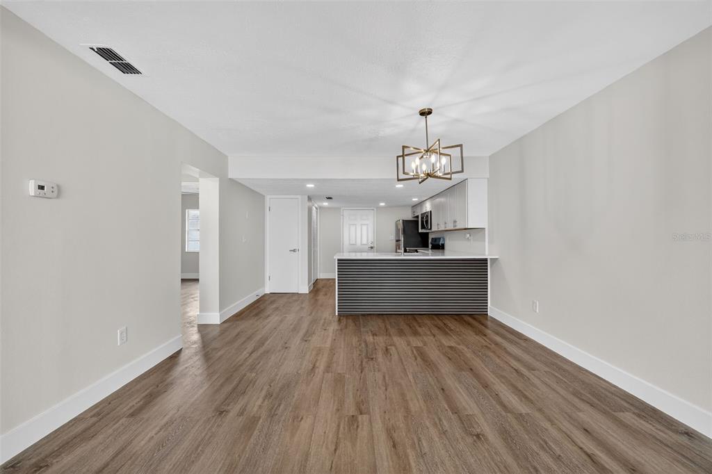 An open-concept living area features wood-look flooring, a kitchen island, and a modern chandelier — 9826 POCONO STREET, PORT RICHEY, FL