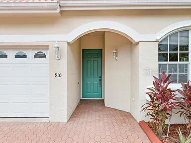The exterior of a house features a white garage door, a teal front door, and landscaping — 910 SW MUNJACK CIRCLE, PORT ST LUCIE, FL