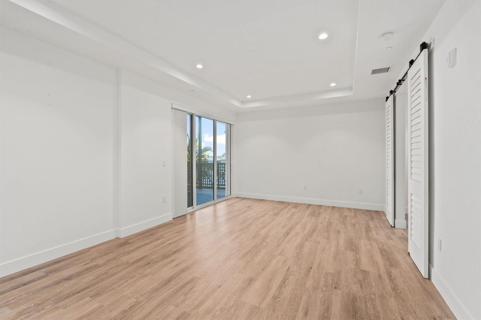 An empty room with light wood-look flooring, white walls, recessed lighting, and a sliding door — 41 SW Seminole Street # 204, Stuart FL 34994, STUART, FL