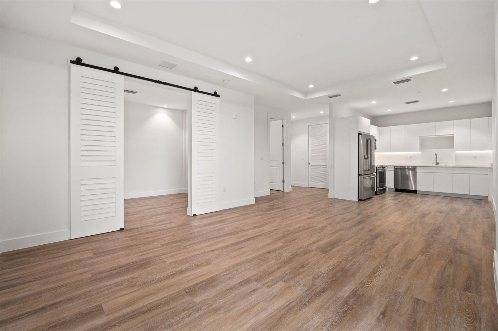 An open-concept living area features white cabinetry, stainless steel appliances, and a sliding barn door — 41 SW Seminole Street # 204, Stuart FL 34994, STUART, FL