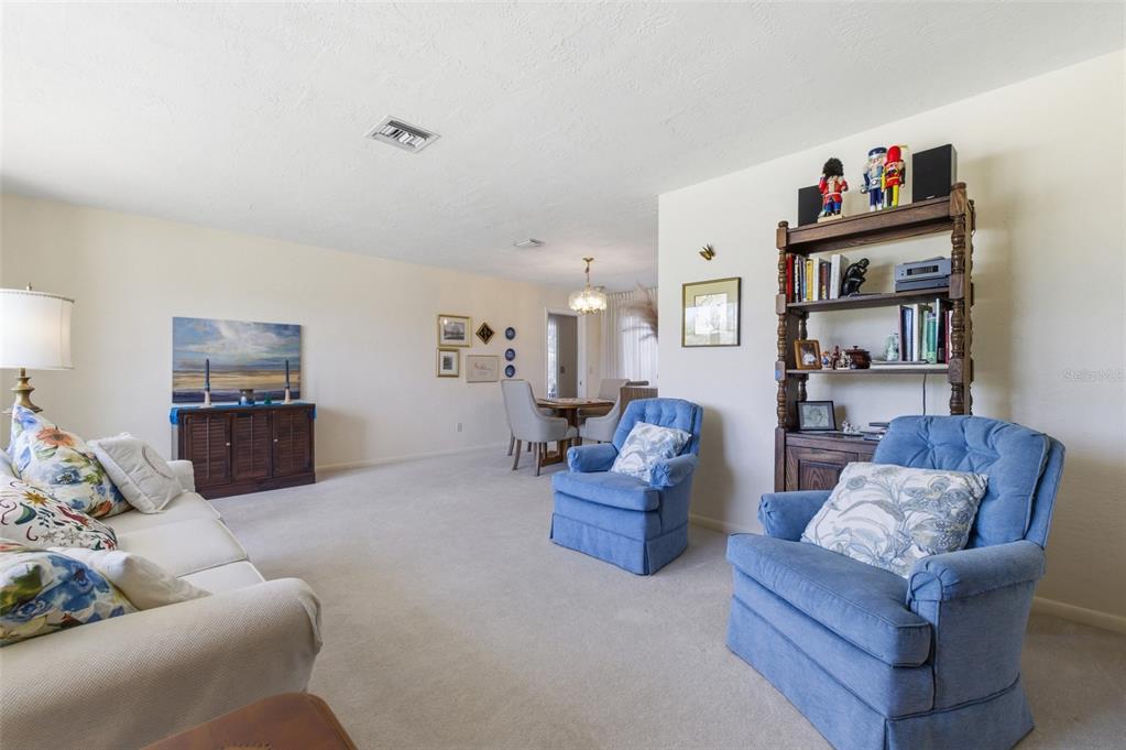 A living room features beige carpet, a white sofa, two blue armchairs, and a bookshelf — 1335 WHISKEY CREEK DRIVE, FORT MYERS, FL