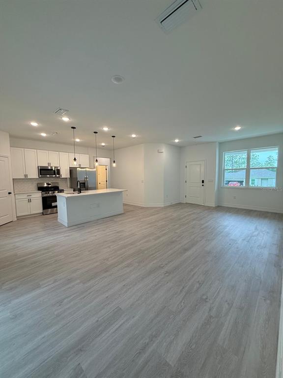 A modern open-concept kitchen features white cabinetry, a central island, and light wood-look flooring — 9481 N STAFFORD DRIVE, CITRUS SPRINGS, FL