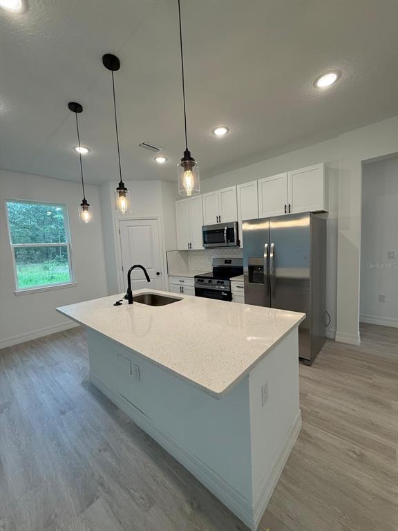 A modern kitchen features white cabinets, a quartz-topped island, stainless steel appliances, and pendant lighting — 9481 N STAFFORD DRIVE, CITRUS SPRINGS, FL
