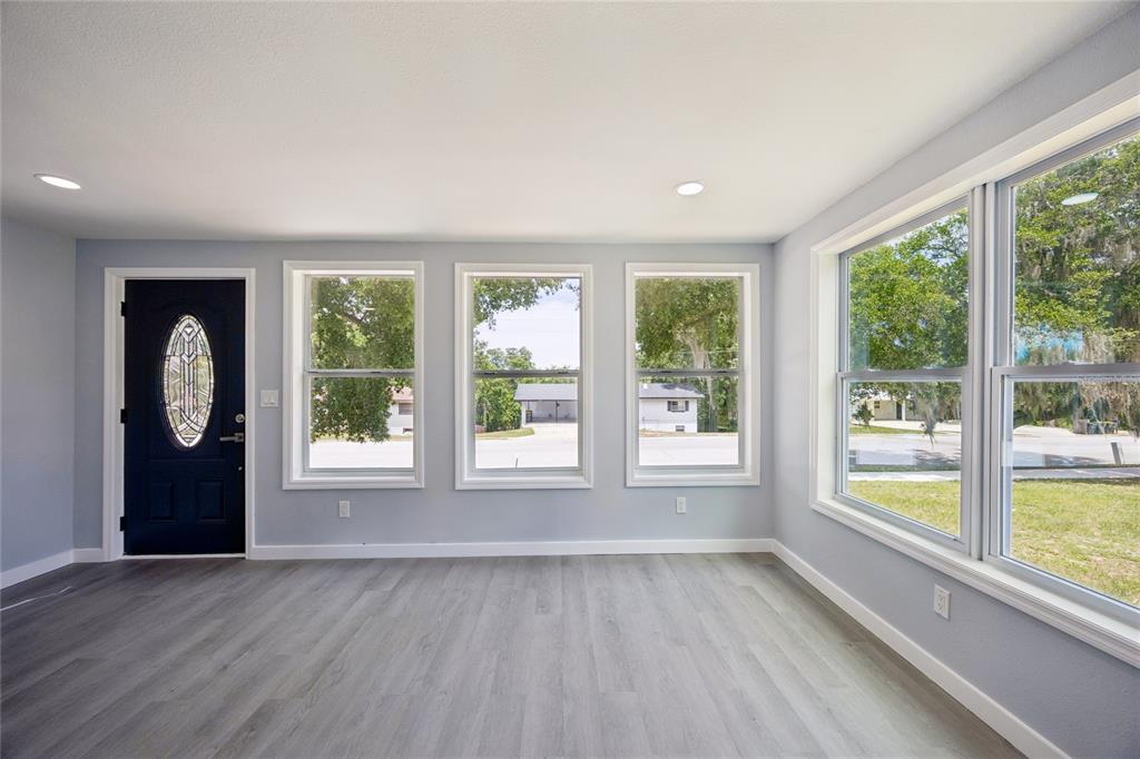 A bright room features light gray walls, wood-look flooring, a dark front door, and multiple windows — 1326 EAST AVENUE, CLERMONT, FL